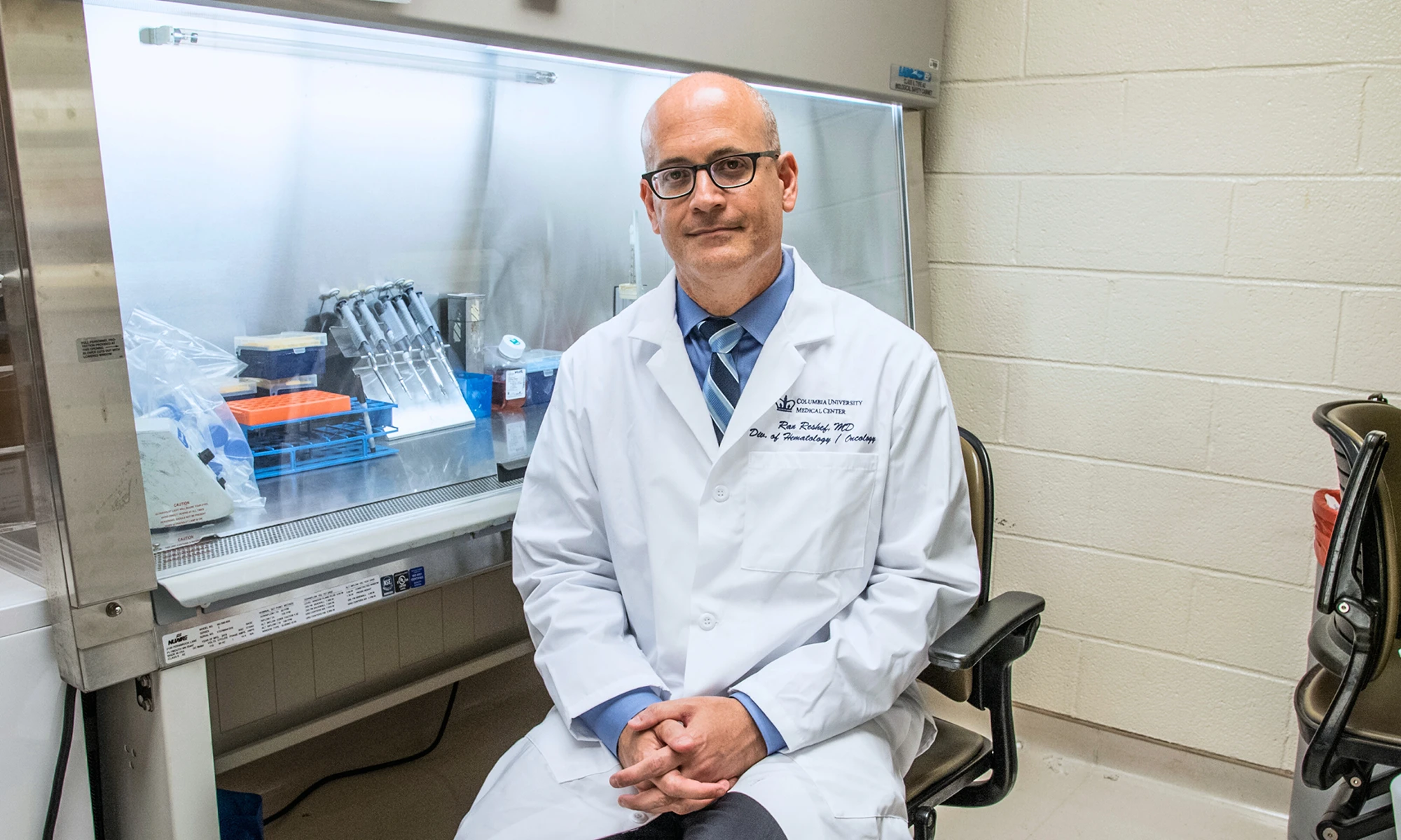 Ran Reshef is sitting on a chair with some lab equipment in the background.