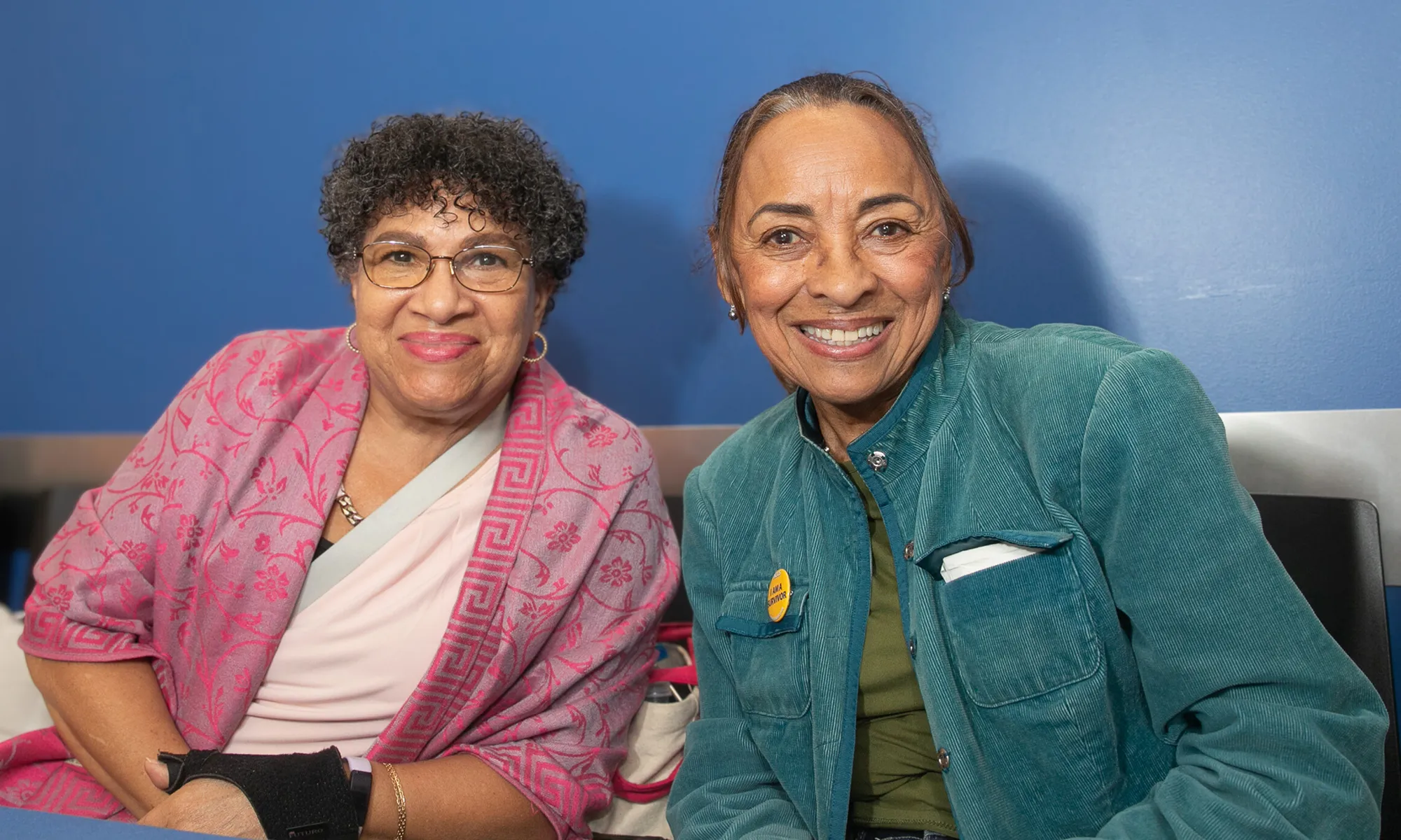 Two women sit side by side smiling at the camera during HICCC’s Cancer Survivors Month event, celebrating community and resilience.