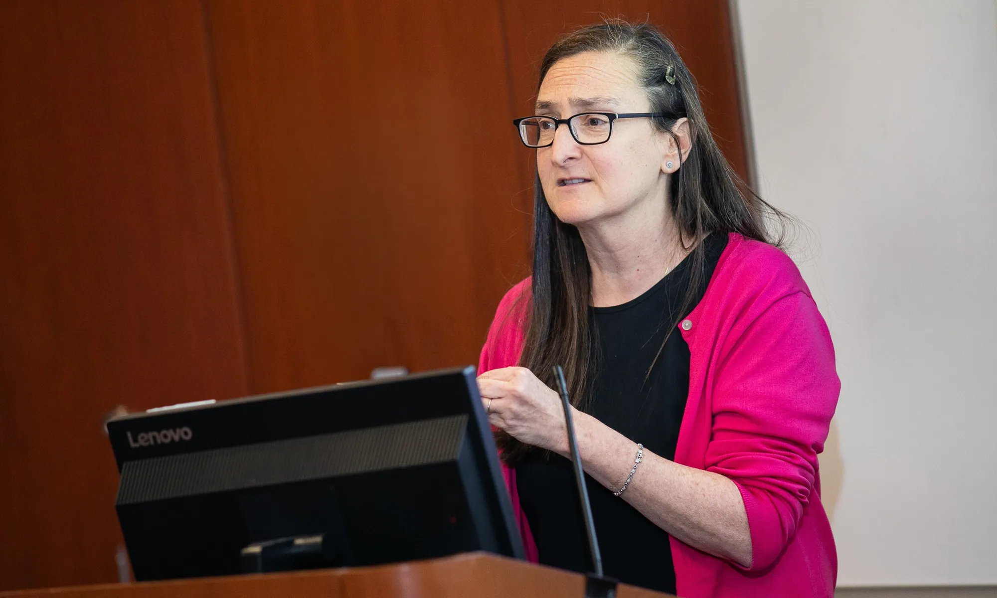 Dawn Hershman, MD, MS, FASCO, speaks at the podium during the HICCC’s inaugural Cancer Survivors Month event, wearing a bright pink cardigan and glasses as she addresses the audience.